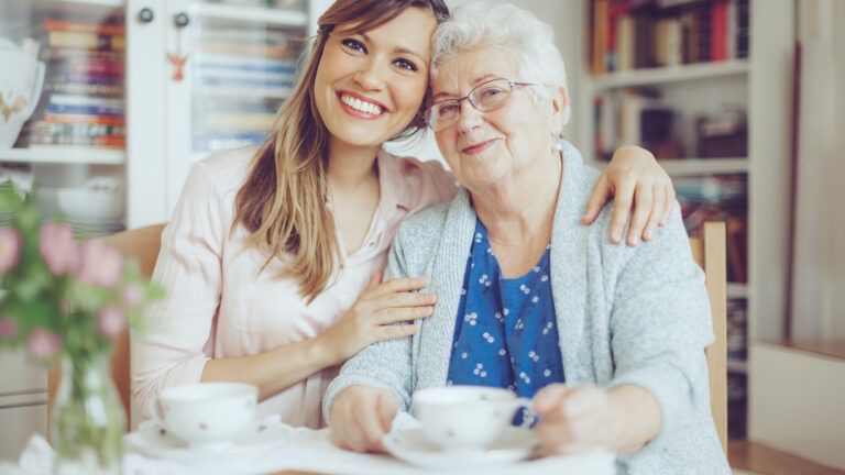 A caregiving having tea with an aging woman; Getty Images