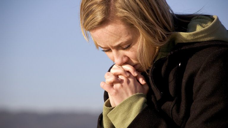 A woman clasps her hands in prayer