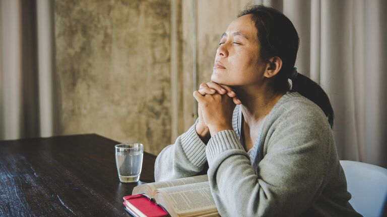 A woman clasps her hands in prayer